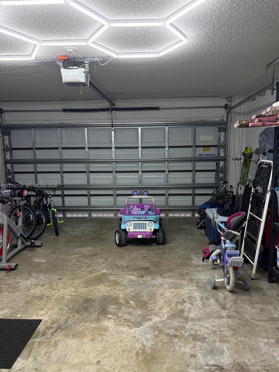 Garage space featuring a paneled sectional door, concrete flooring, and an installed hexagonal LED ceiling light fixture Garage space featuring a paneled sectional door, concrete flooring, and an installed hexagonal LED ceiling light fixture