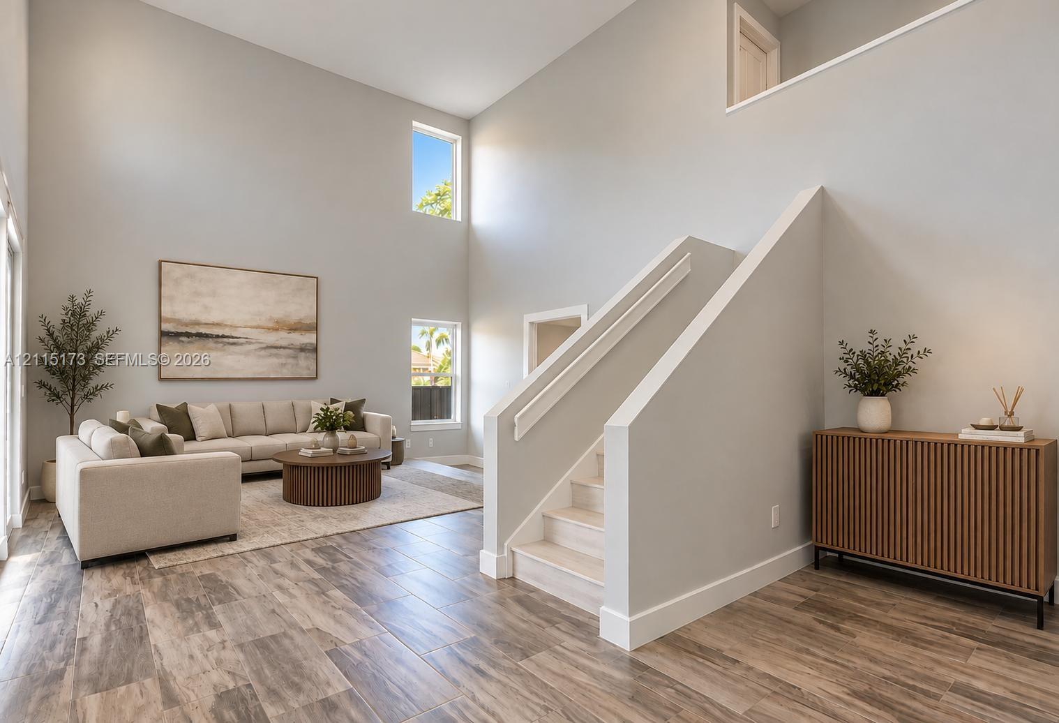 High-ceiling interior featuring wood-finish flooring, staircase with a solid-panel railing, and multiple vertical windows High-ceiling interior featuring wood-finish flooring, staircase with a solid-panel railing, and multiple vertical windows