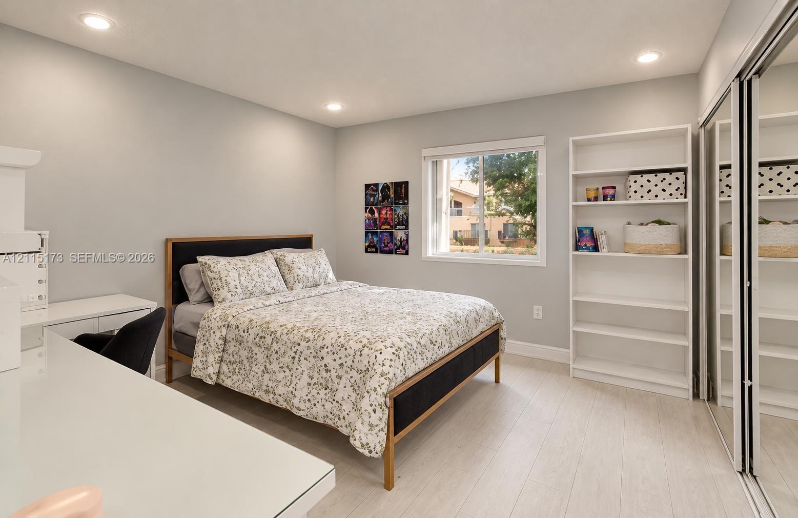 Room featuring wood-finish flooring, recessed lighting, a single-hung window, built-in shelving, and a dual-panel mirrored sliding closet Room featuring wood-finish flooring, recessed lighting, a single-hung window, built-in shelving, and a dual-panel mirrored sliding closet
