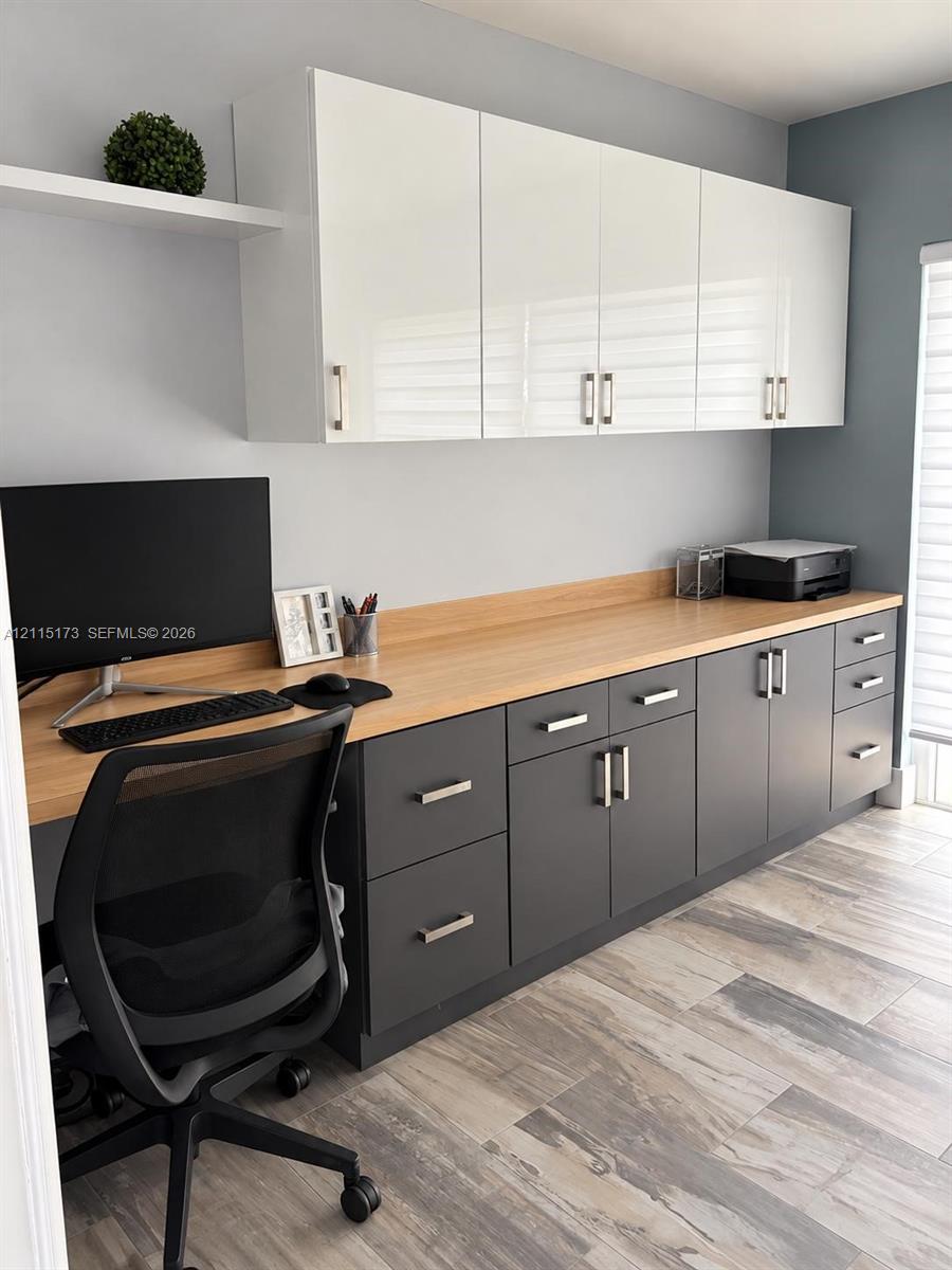 Built-in cabinetry featuring white gloss upper cupboards, charcoal lower drawers and cabinets, wood-finish countertop, floating display shelf, and light-tone wood-finish flooring