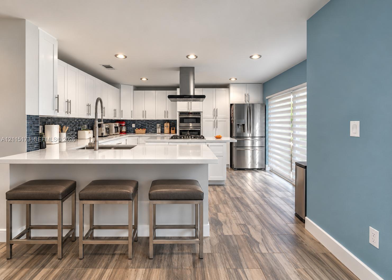 Kitchen featuring white shaker-style cabinetry, white quartz countertops, stainless steel appliances, a mosaic tile backsplash, and wood-finish flooring