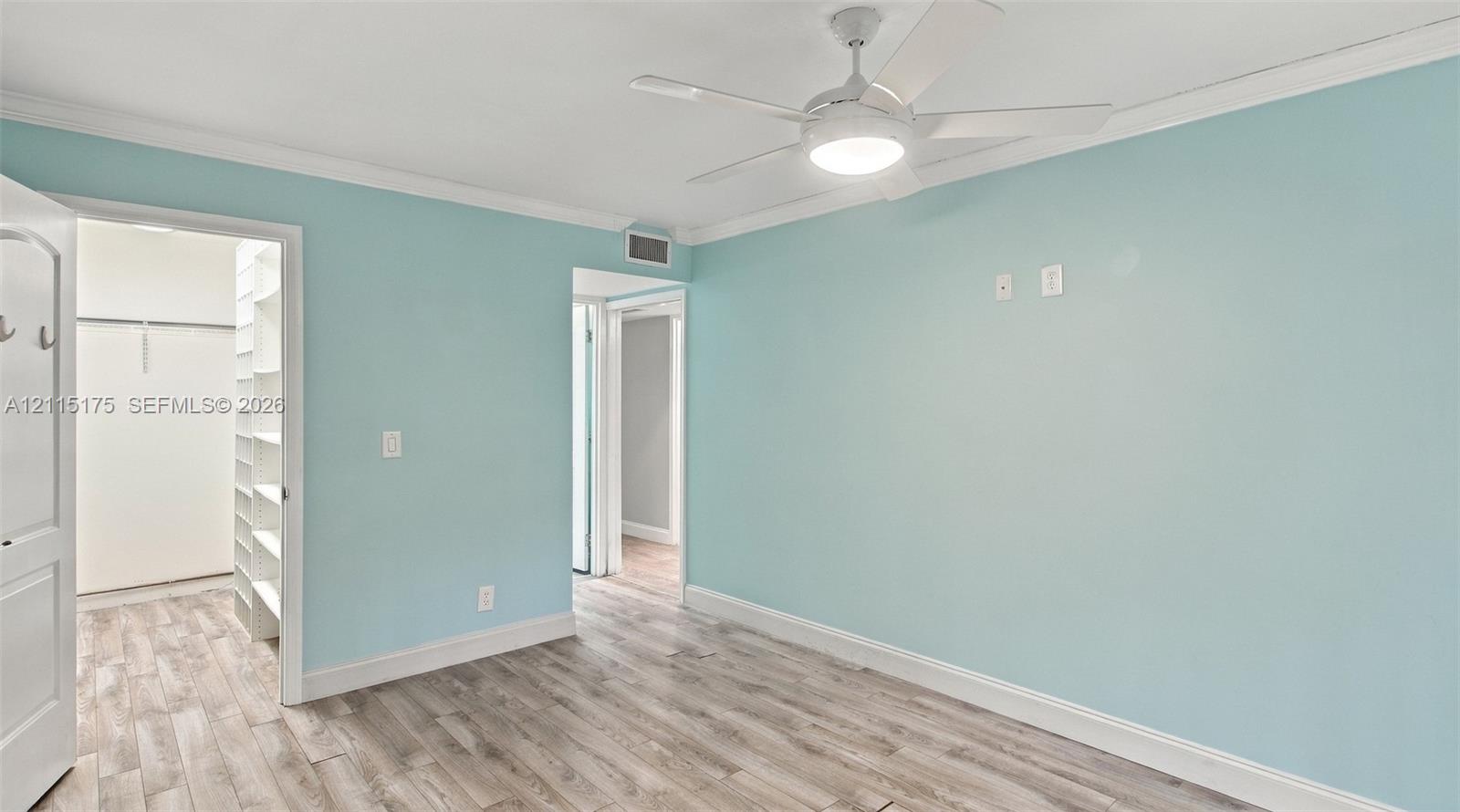 Room featuring wood-finish flooring, crown molding, a ceiling fan with integrated lighting, and a walk-in closet with built-in shelving