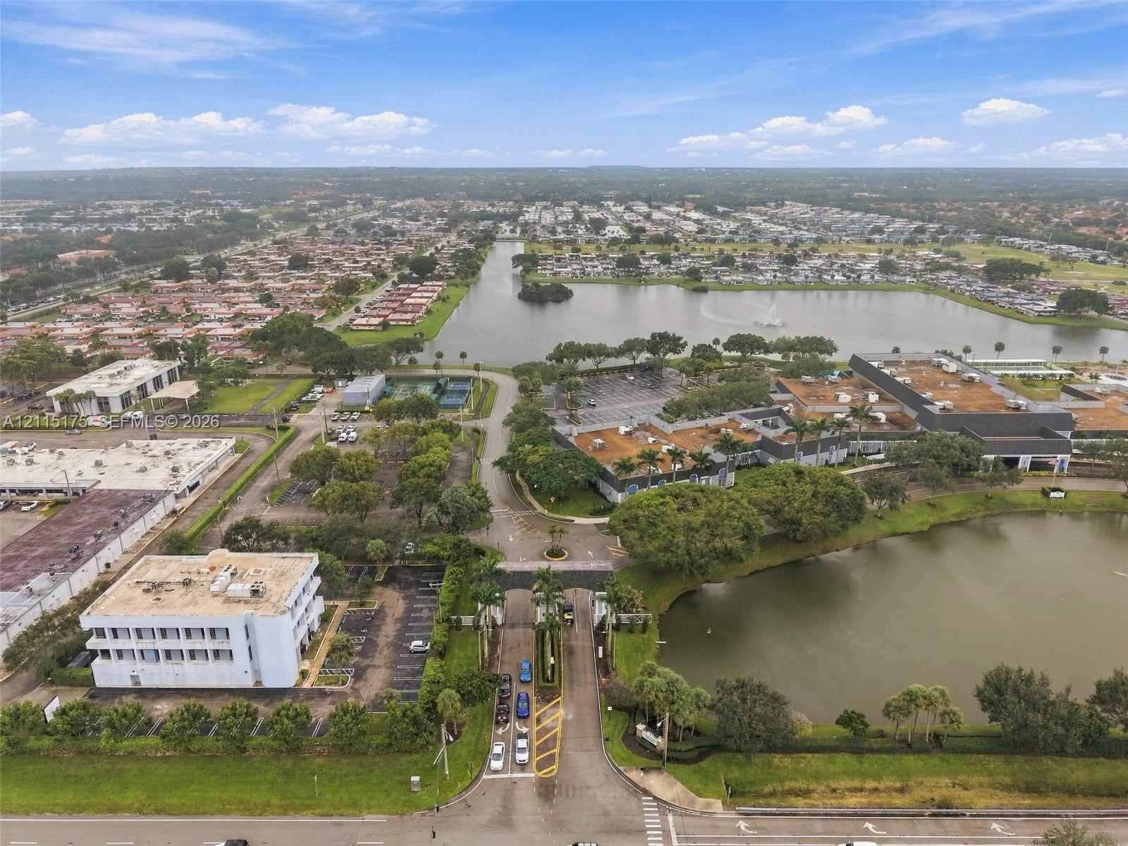 Aerial perspective showing one of the main entrances featuring gated access, expansive water frontage, mature trees, and the main clubhouse on the righ