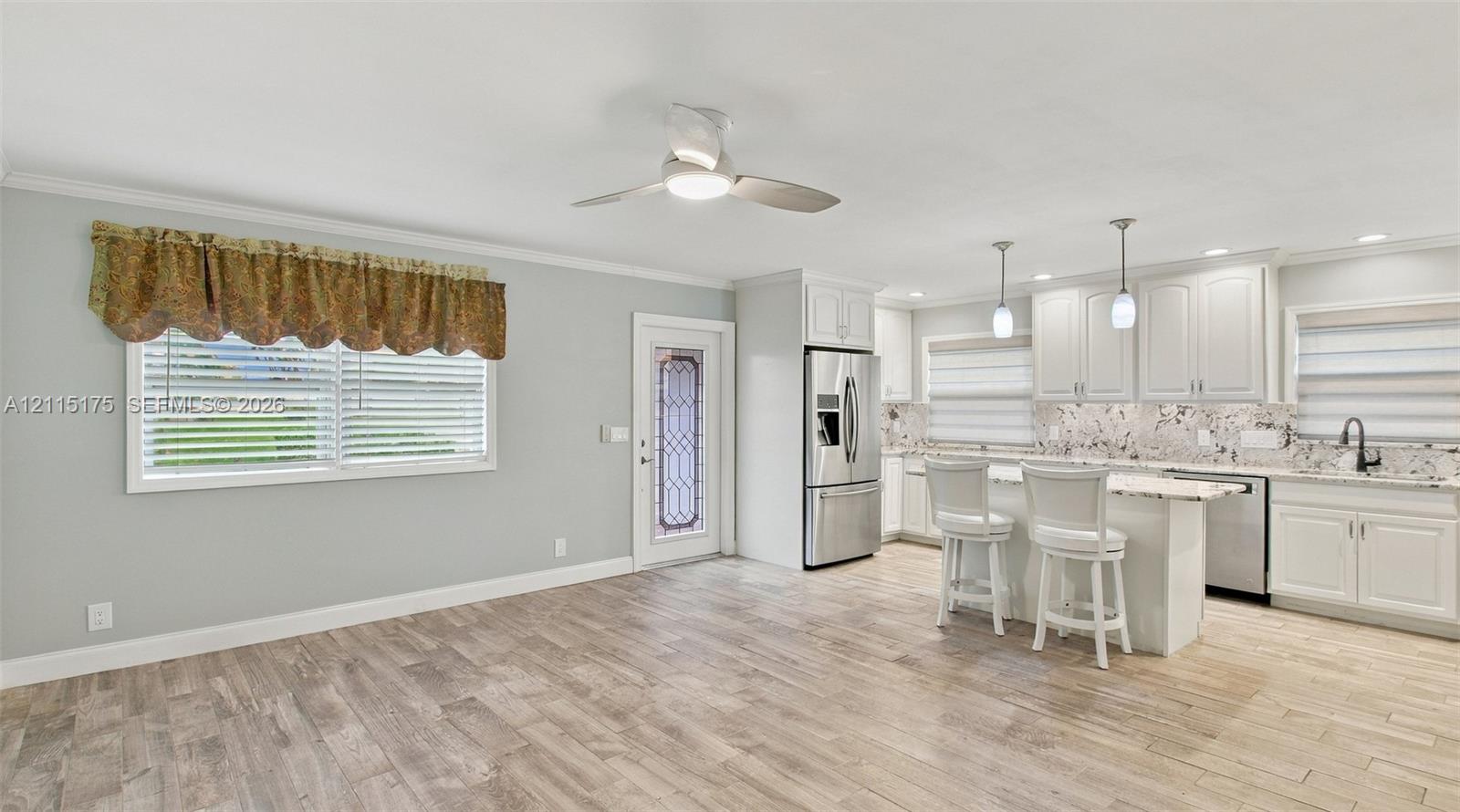 Open-concept interior featuring wood-finish tile flooring, white shaker-style cabinetry, stone-finish countertops, stainless steel appliances, and ceiling-mounted lighting