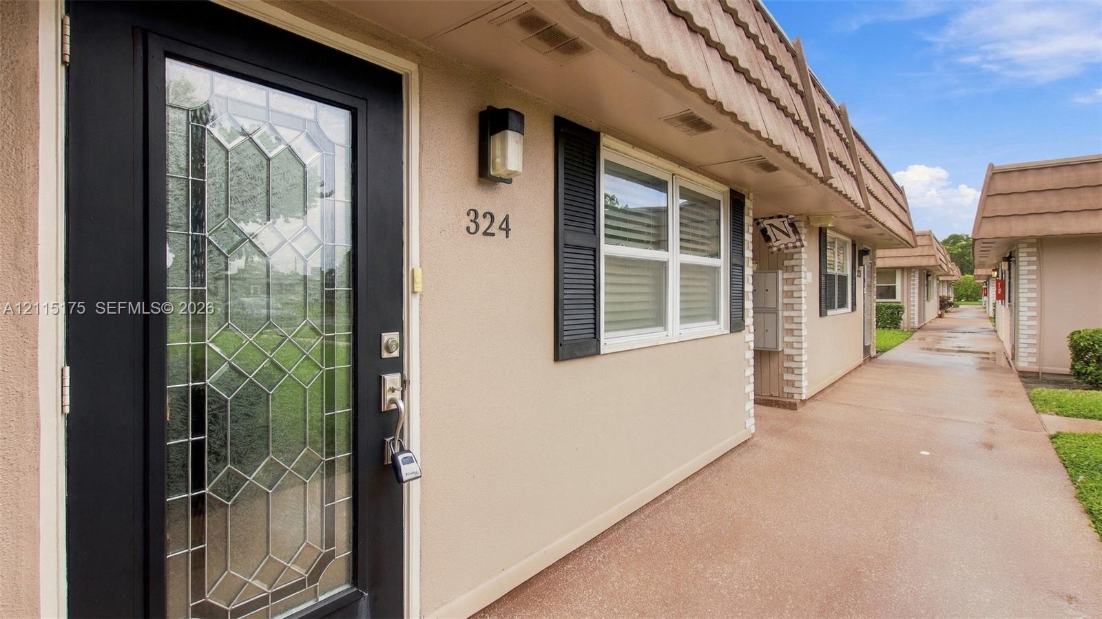 Exterior entry featuring a glass-panel door with decorative leaded accents, dark-framed window shutters, and a concrete walkway