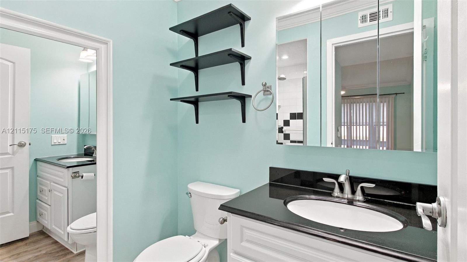 Primary bathroom featuring white cabinetry, a dark stone countertop, an integrated oval sink, and a large mirrored medicine cabinet, complemented by matte black wall-mounted shelving