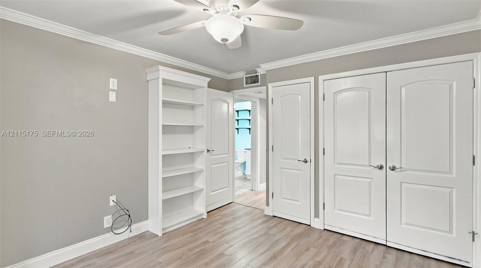 Second bedroom featuring wood-look laminate flooring, crown molding, multi-panel doors for closet, and a ceiling fan with integrated lighting