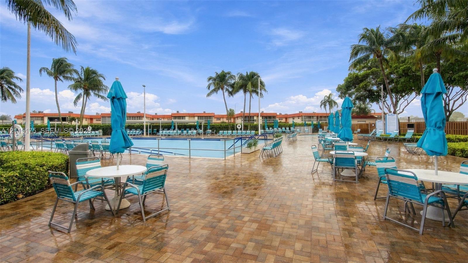 Swimming pool area at one of the satellite clubhouses with paver patio, metal perimeter fencing, and mature palm trees