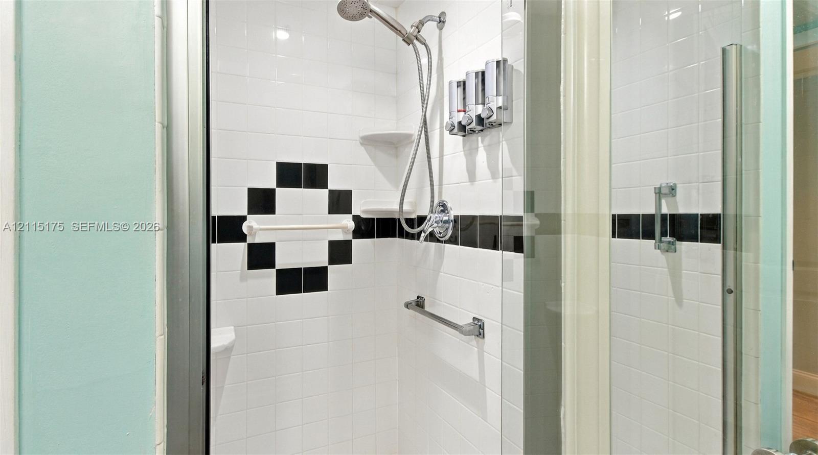 Primary bathroom walk-in shower enclosure featuring white tile, a black accent tile border, built-in corner shelving and a glass door