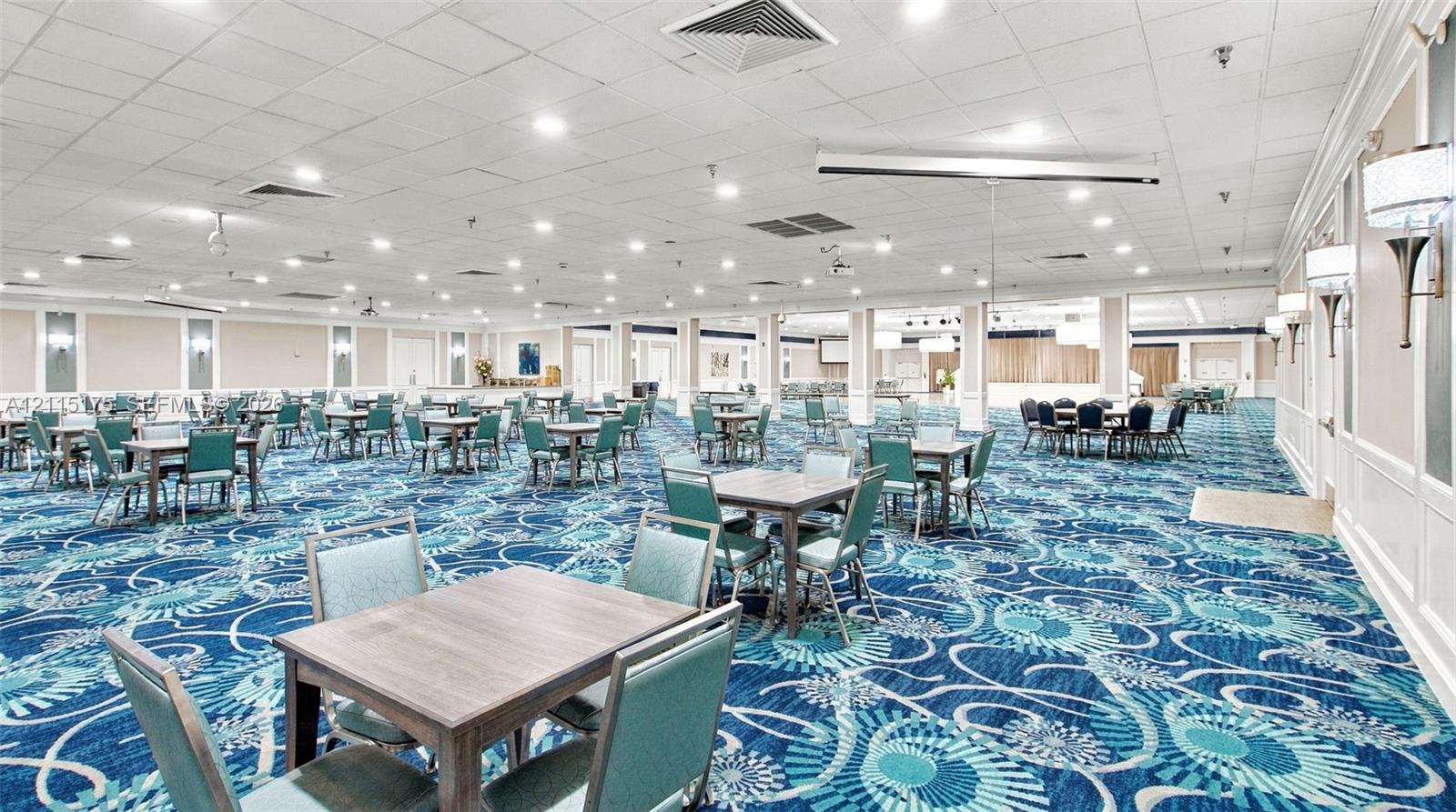 Expansive open-concept room featuring a dance floor, multiple tables, recessed lighting, wall-mounted sconce fixtures, and patterned carpeting for parties and special events