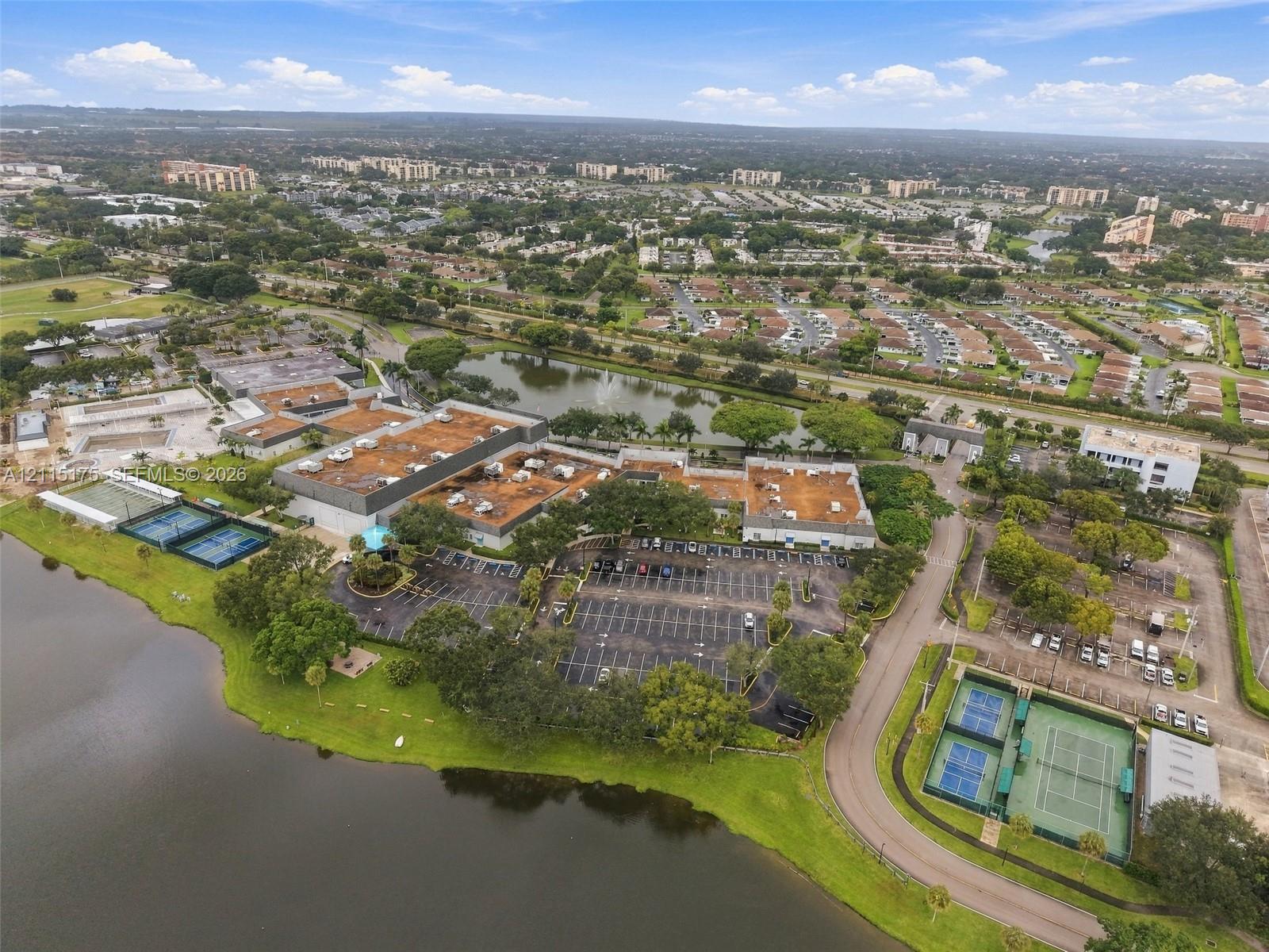 Aerial perspective of the property featuring dual tennis court facilities, expansive waterfront acreage, mature landscaping, and dedicated paved parking areas