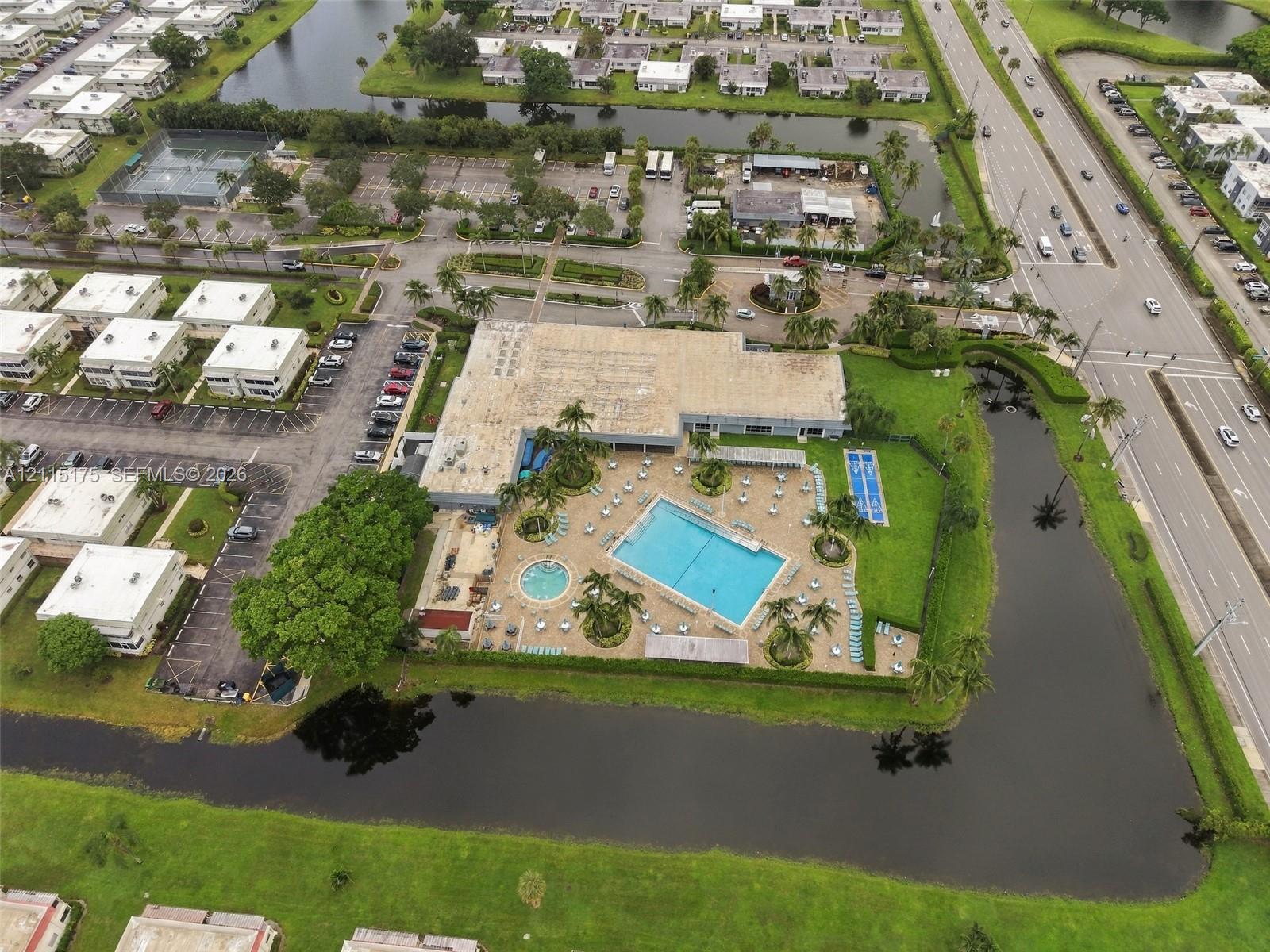 Aerial perspective of community facilities featuring a swimming pool, spa, surrounding paved patio, dedicated sports court, and perimeter canal