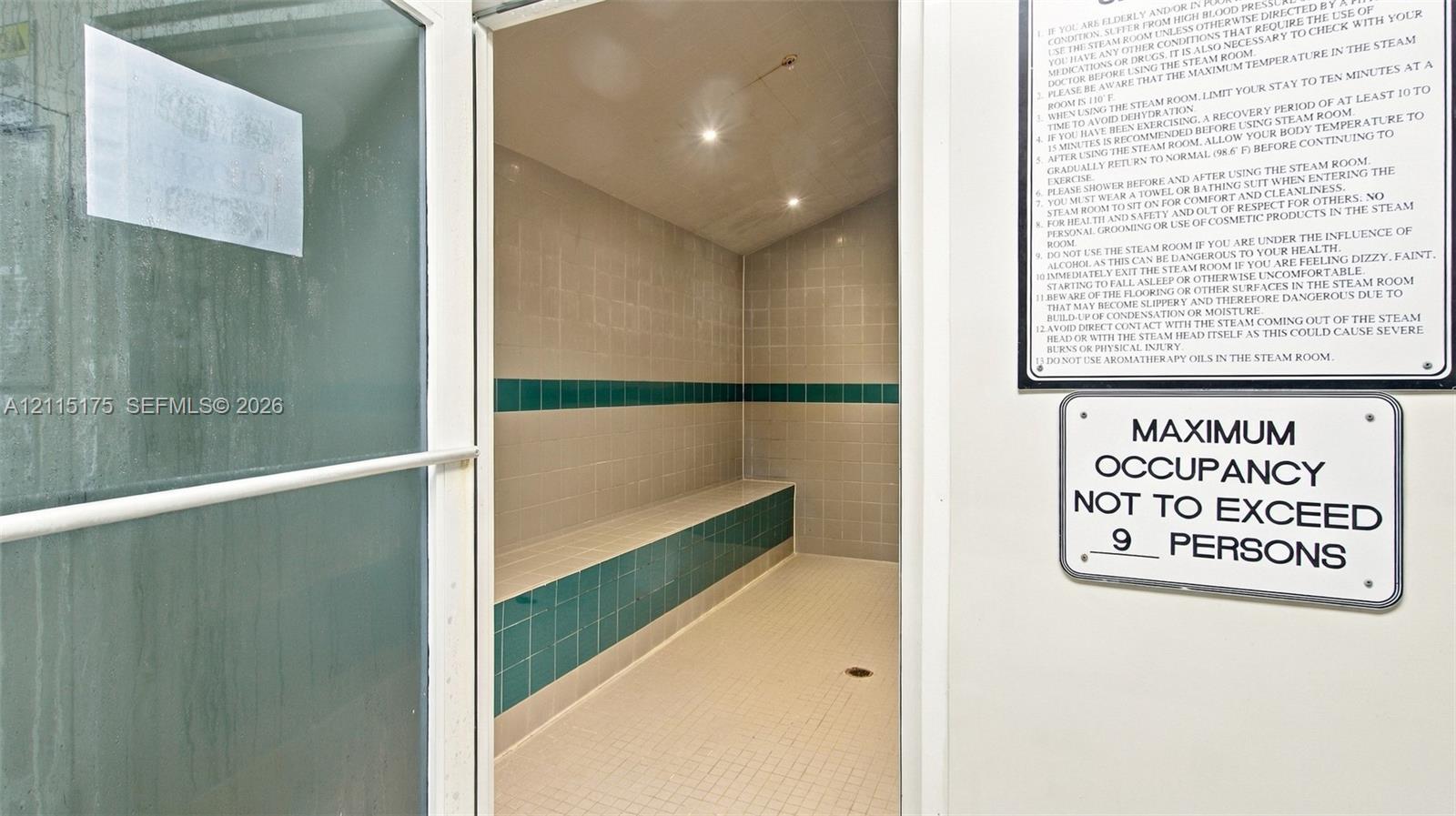 Steam room featuring tile flooring, built-in tiered seating, wall-mounted recessed lighting, and a glass-paneled entry door