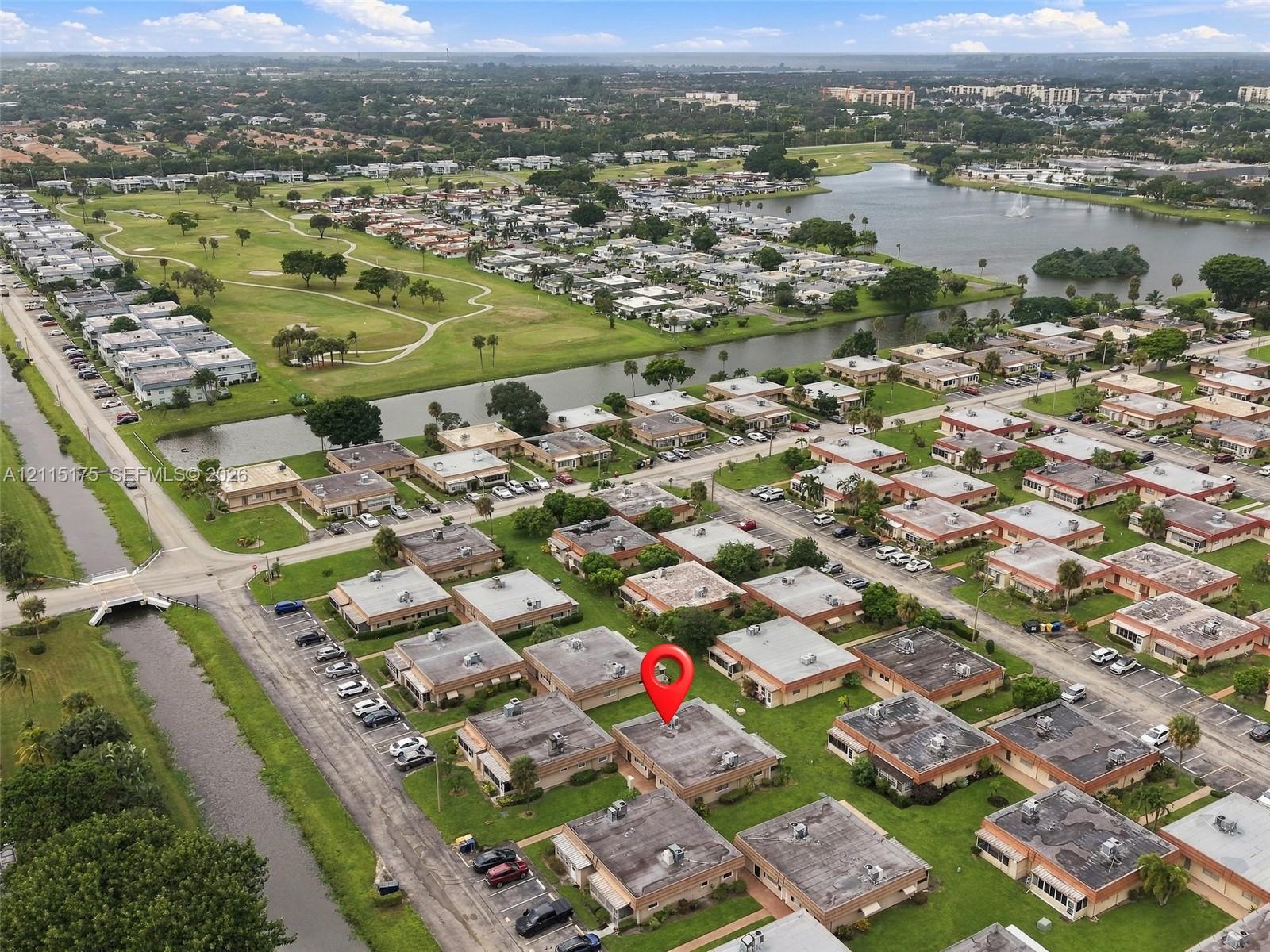 Aerial perspective of a single-story residence situated within a planned community, featuring a flat roof and proximity to a waterway and expansive green space
