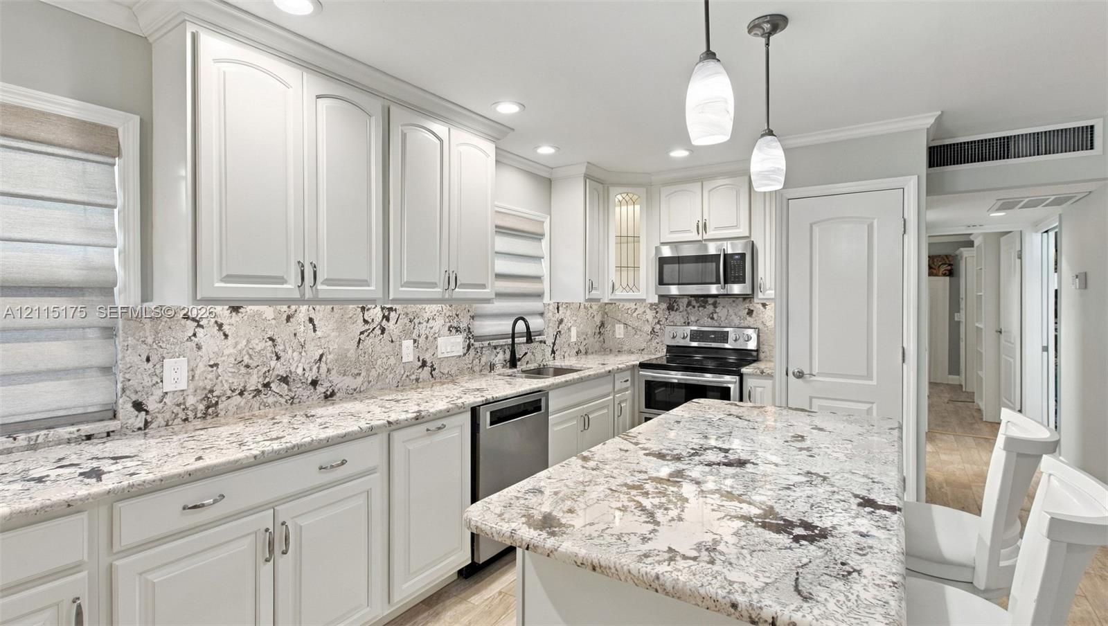 Open-concept kitchen featuring white shaker-style cabinetry, quartz countertops, stainless steel appliances, pendant lighting, and porcelain tile wood-look flooring