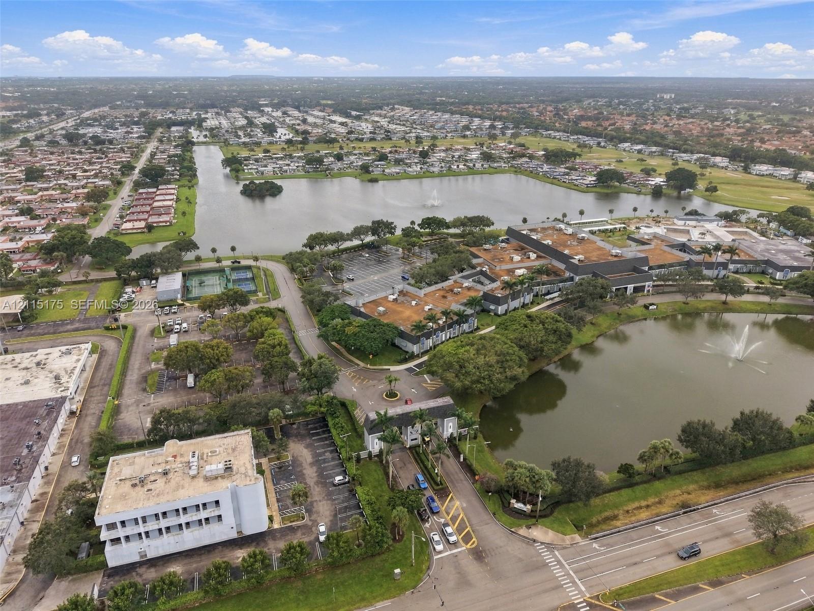 Aerial perspective of a multi-structure property featuring expansive water frontage, multiple decorative fountains, tennis courts, and landscaped grounds