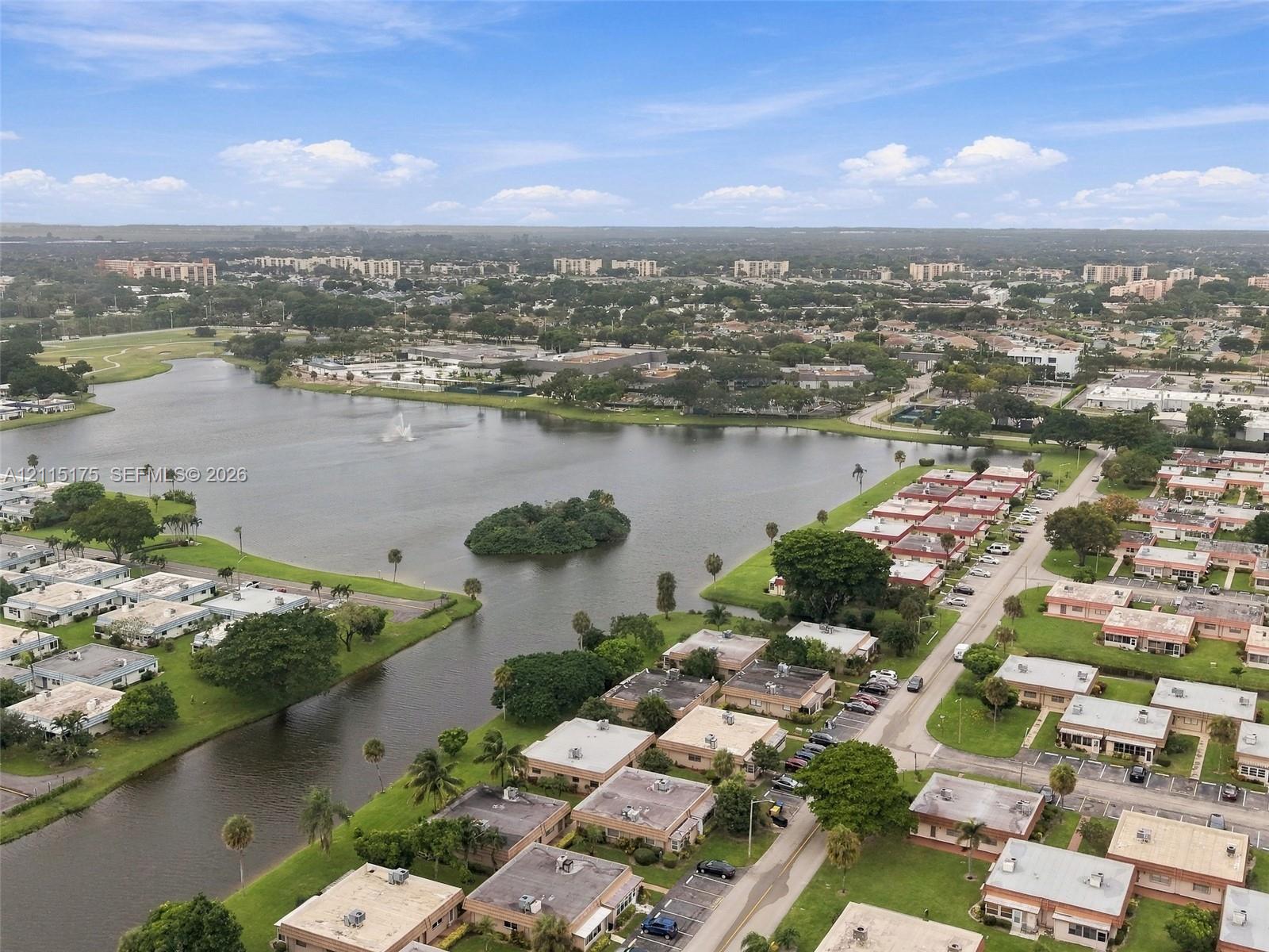 Aerial perspective of a multi-unit residential community featuring a large central lake, manicured green space, and mature palm trees