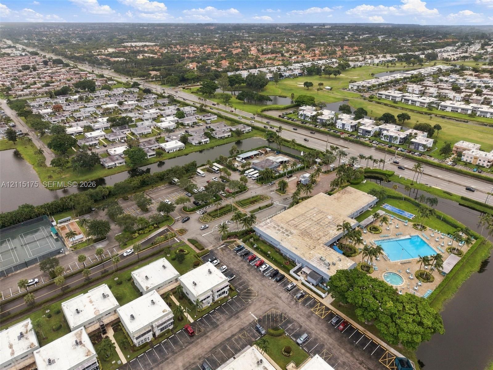 Aerial perspective featuring a swimming pool, multiple tennis courts, paved parking areas, and mature landscaping