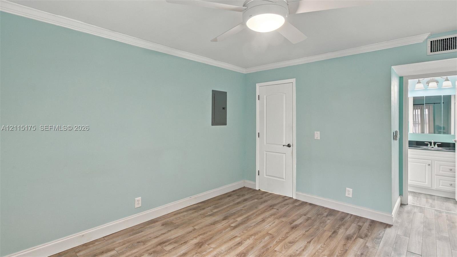 Primary bedroom featuring laminate flooring, crown molding, a ceiling fan with integrated lighting, and a solid-core interior door to a walk-in closet