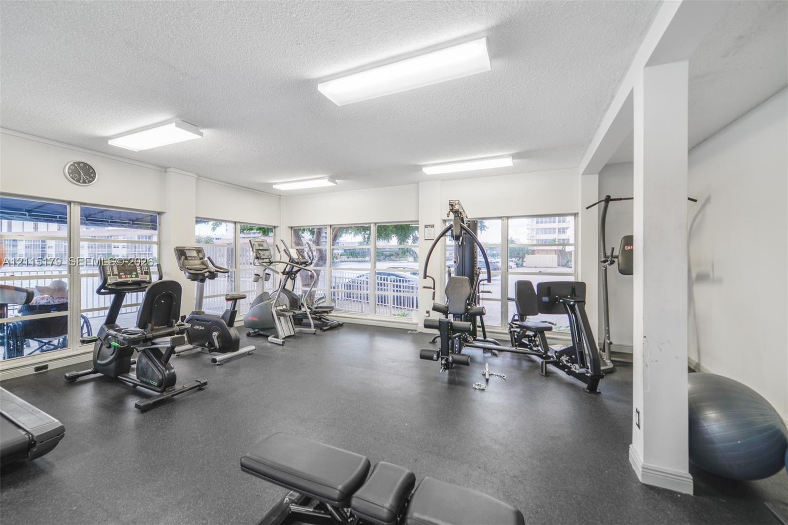 Fitness room featuring rubberized flooring, expansive windows, and overhead fluorescent lighting