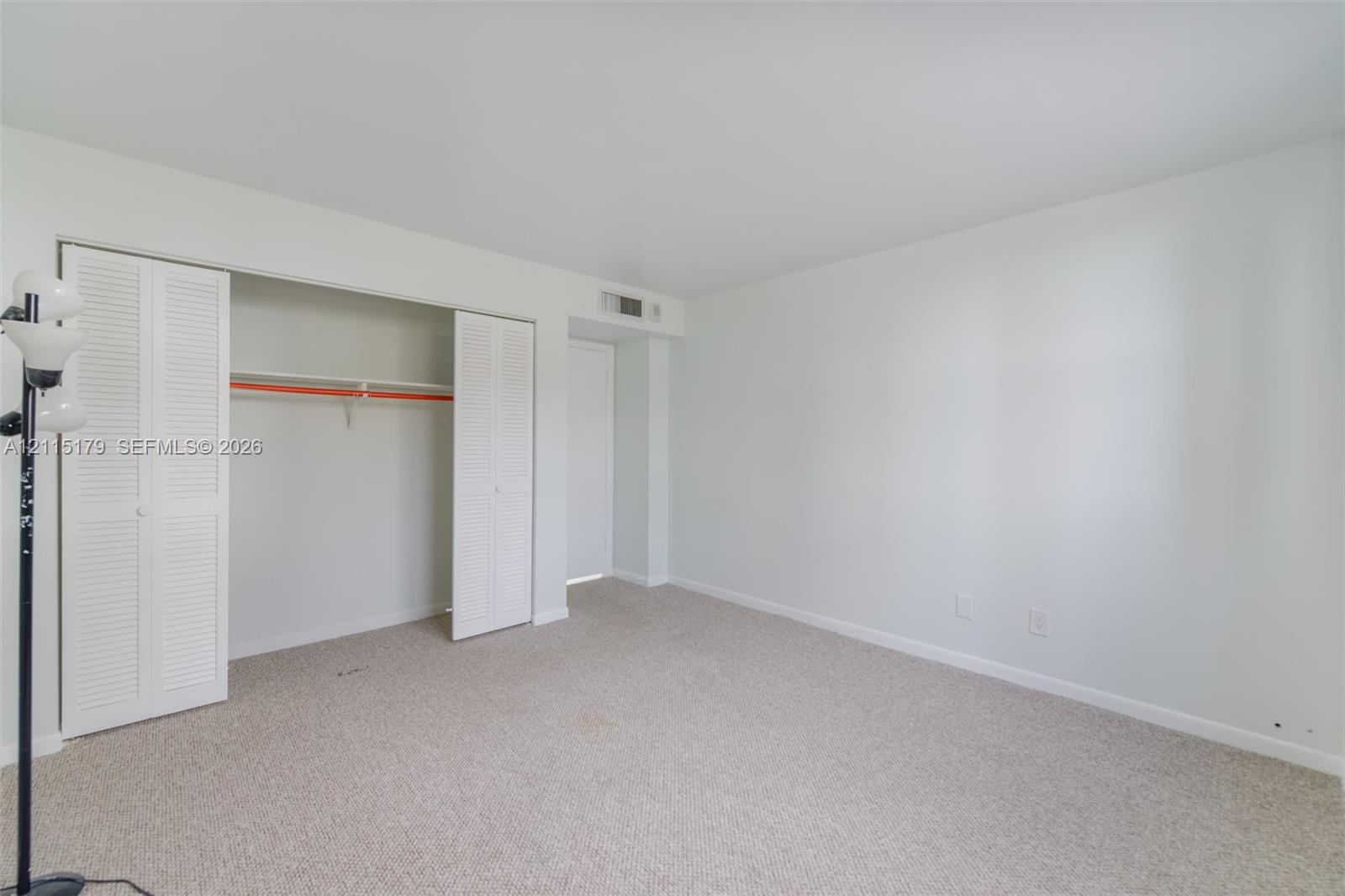 Neutral-toned interior featuring wall-to-wall carpeting, white walls, and a closet with bifold louvered doors