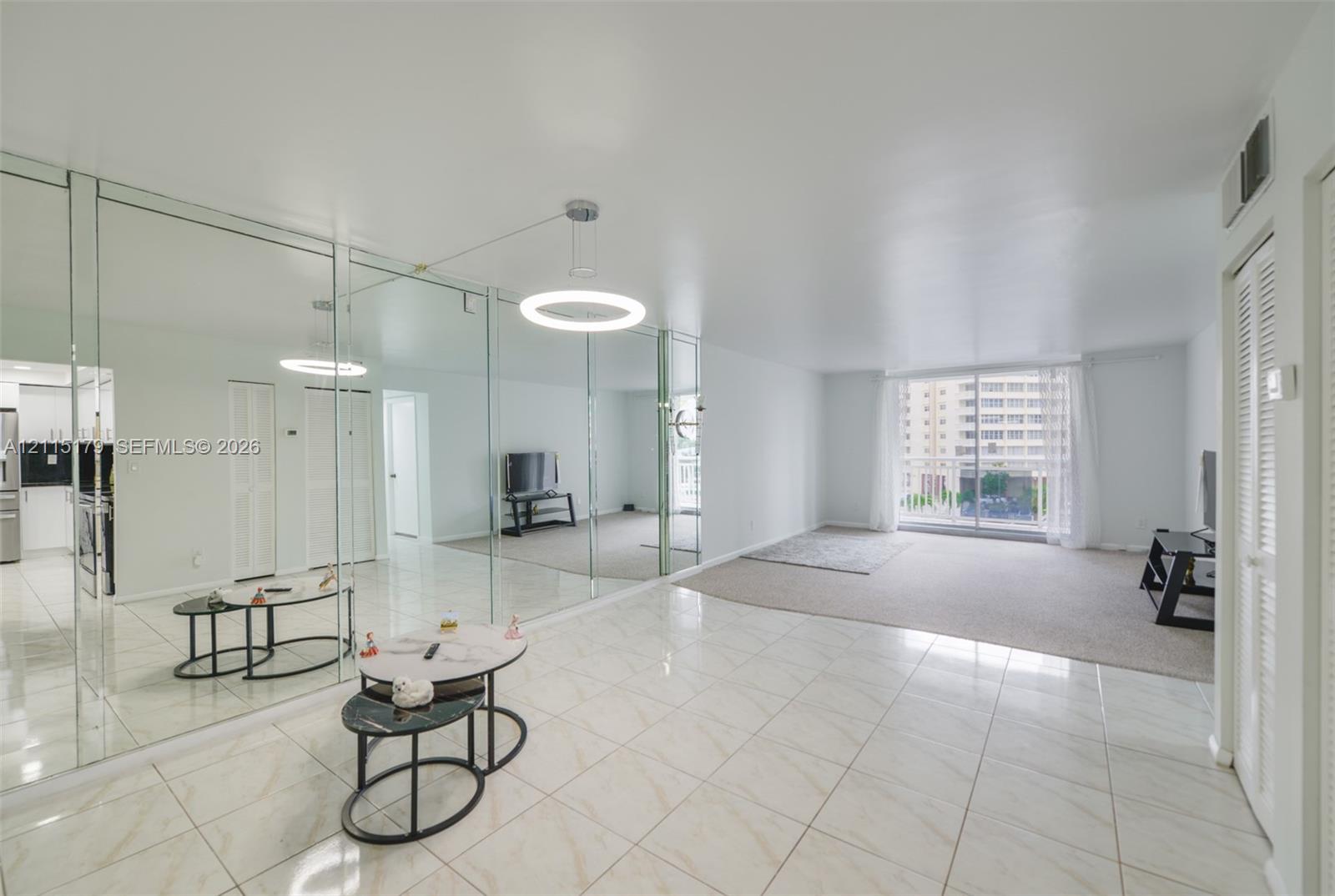 Spacious interior featuring full-wall mirrored paneling, polished light-tone tile flooring, neutral carpeting, and a modern circular LED pendant light fixture