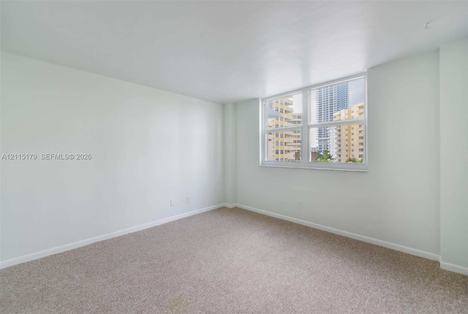 Interior space featuring neutral wall tones, wall-to-wall carpeting, and a large multi-pane window with urban exterior surroundings
