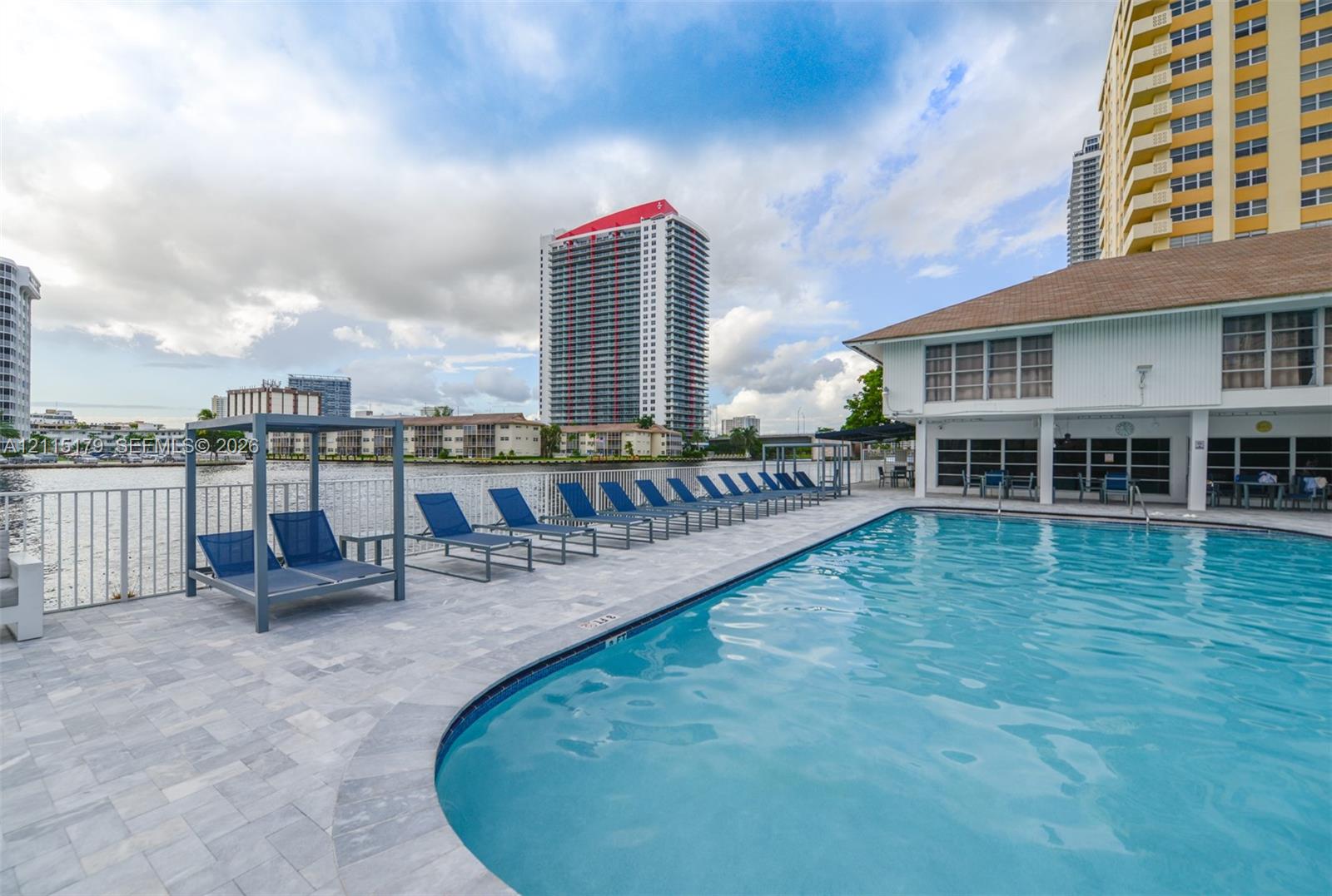 Waterfront swimming pool featuring paver decking, metal perimeter fencing, and a built-in metal frame cabana structure