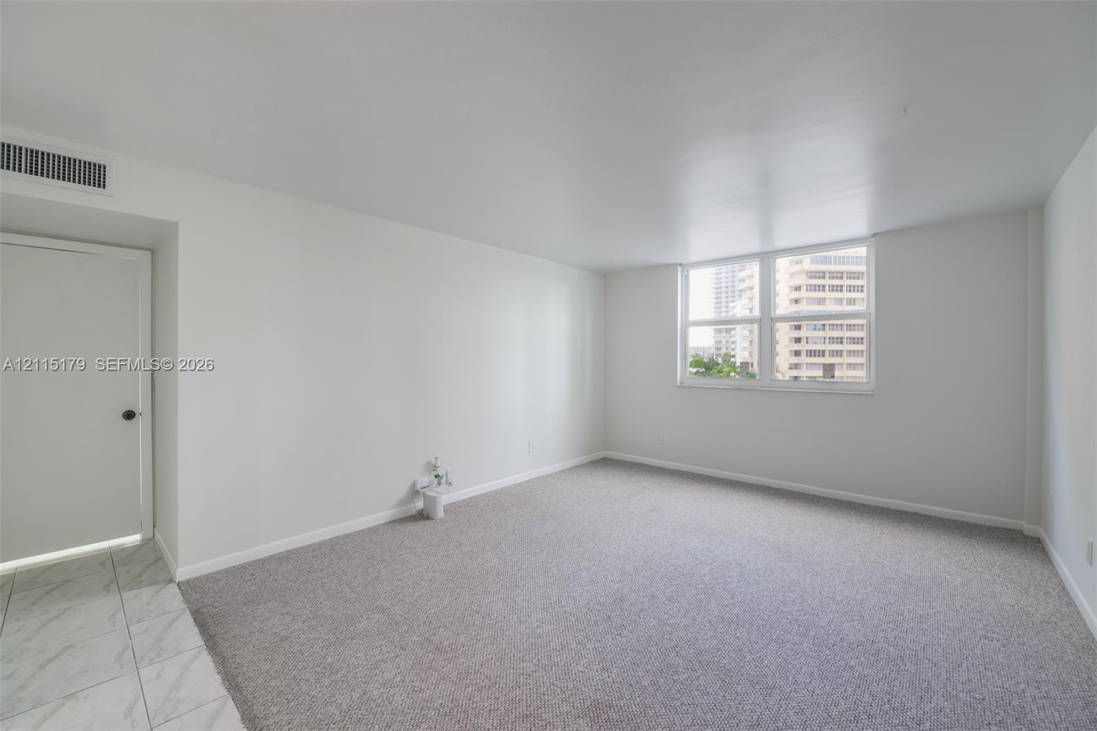 Neutral-toned interior space featuring light-colored wall-to-wall carpeting, white walls, and a large multi-pane window