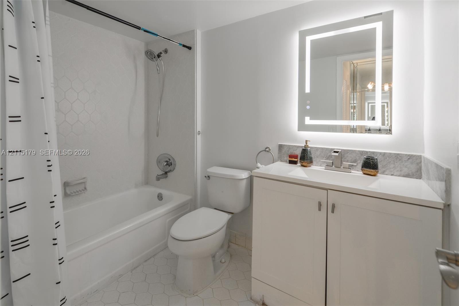 Bathroom featuring a white vanity cabinet with a stone-top integrated sink, a rectangular backlit mirror, and a tiled shower enclosure with a geometric pattern
