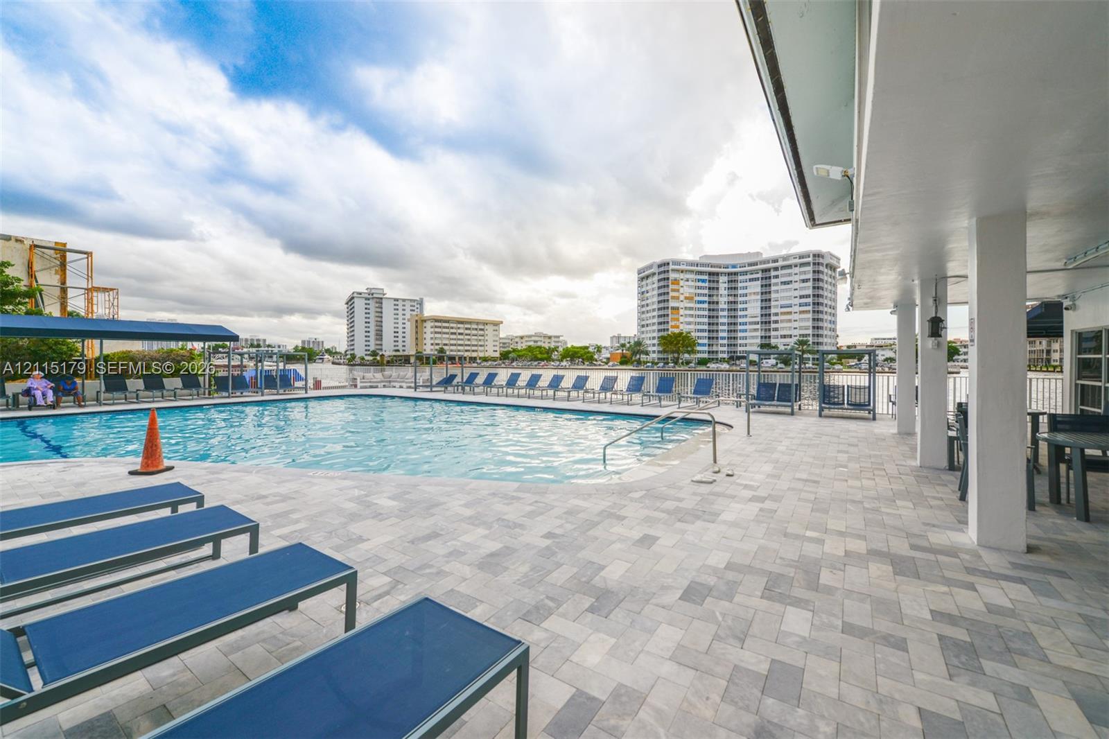 In-ground swimming pool featuring a herringbone-patterned stone paver deck and a covered patio area