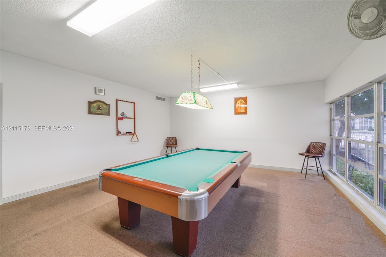 Expansive interior room featuring floor-to-ceiling windows, wall-to-wall carpeting, and a dual-pendant billiard light fixture
