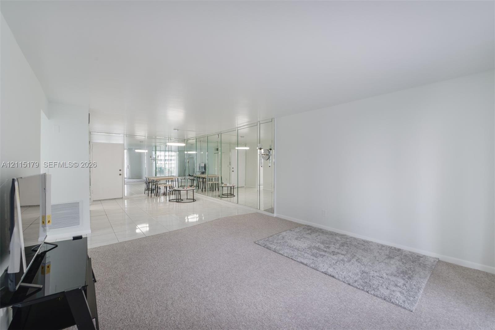 Open-concept interior featuring light-toned carpeting, glossy tile flooring, and wall-to-wall mirrored paneling