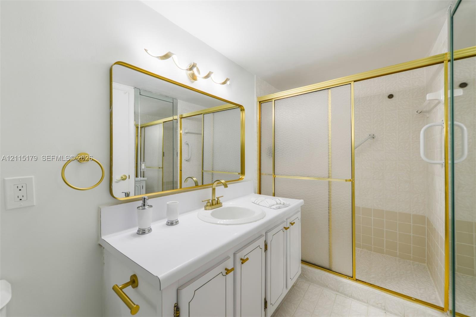 Bathroom vanity with a white countertop, inset sink, brass-tone hardware, and an expansive wall-mounted mirror