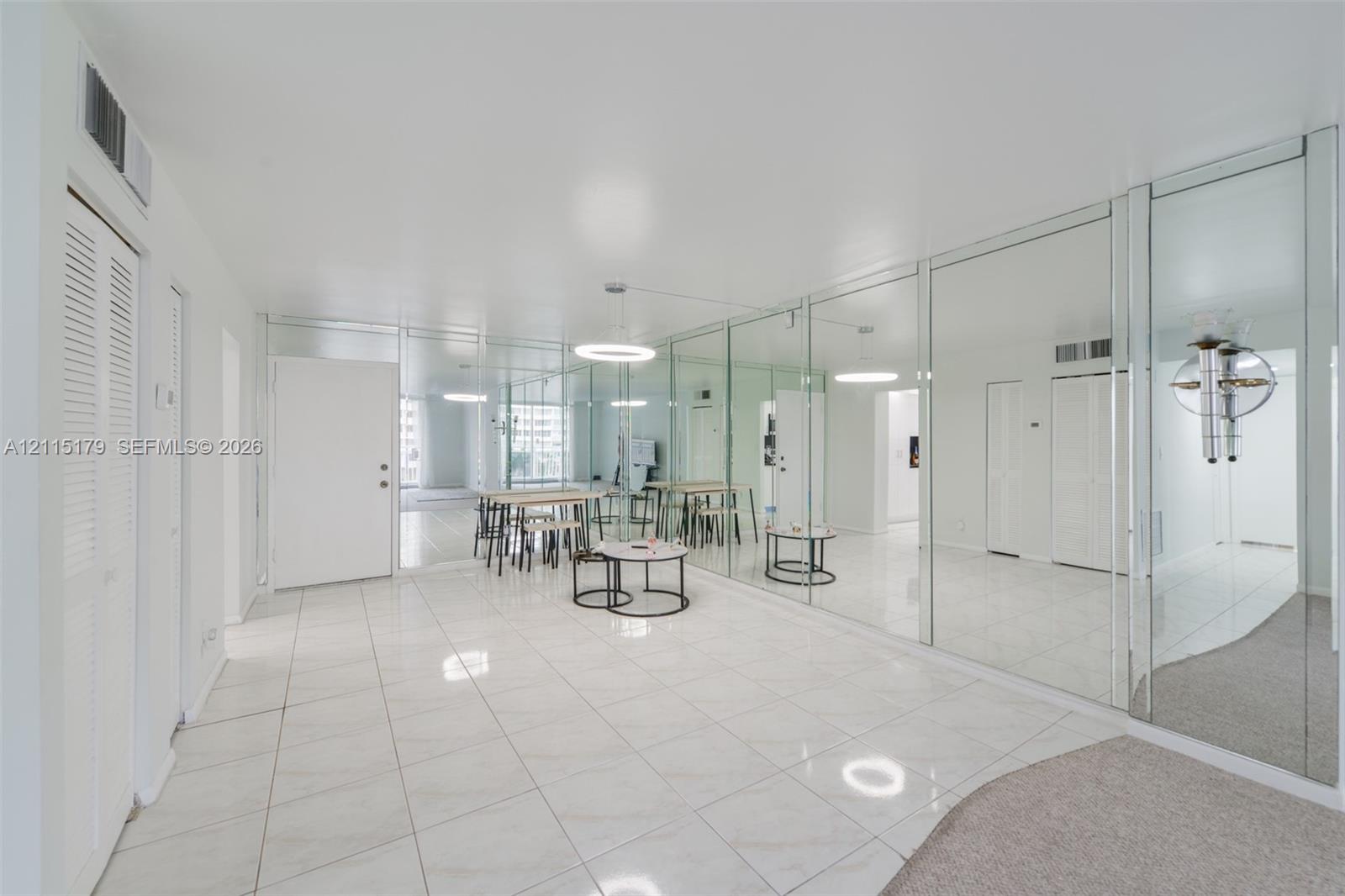 Glossy tile flooring, wall-to-wall mirrored paneling, recessed circular lighting fixtures, and louvered-door closets