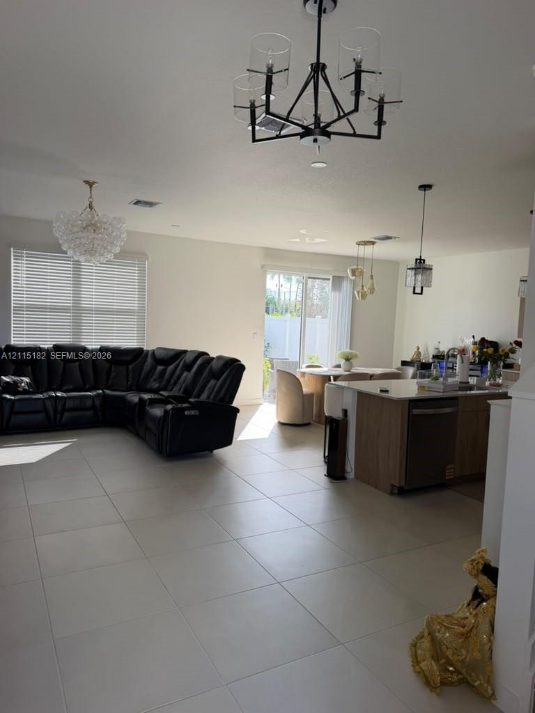 Open floor plan featuring large-format tile flooring, a kitchen island with stone countertops, sliding glass patio doors, and multi-light chandelier fixtures