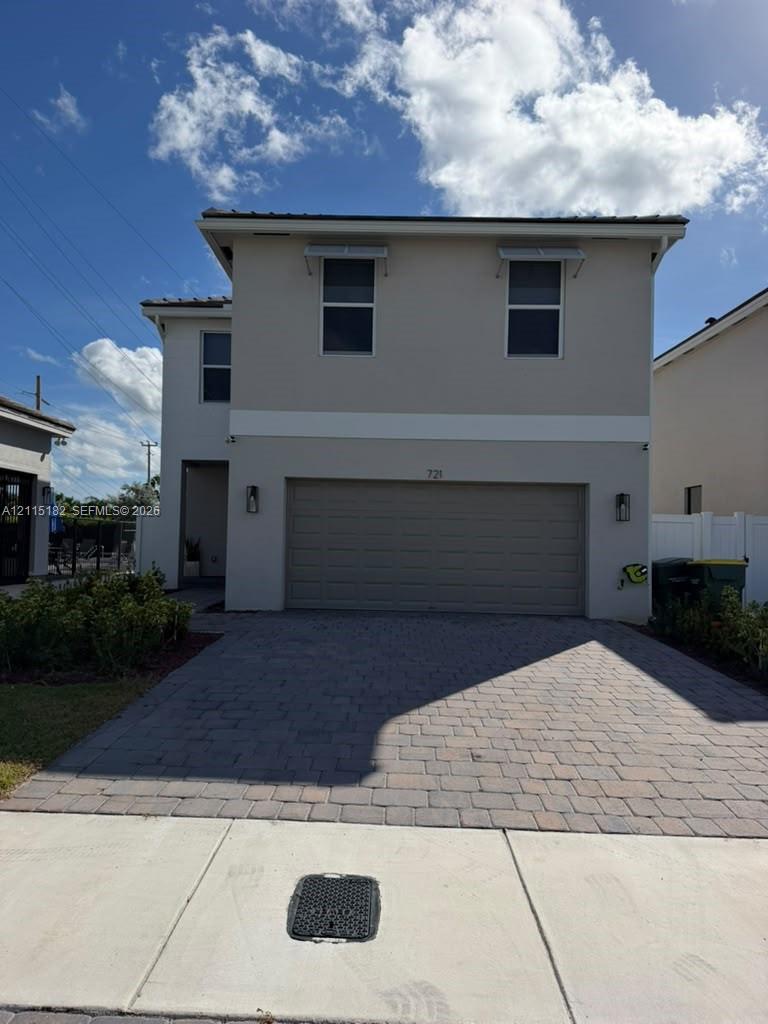 Two-story exterior featuring a paver driveway, two-car garage, and upper-level window awnings Two-story exterior featuring a paver driveway, two-car garage, and upper-level window awnings