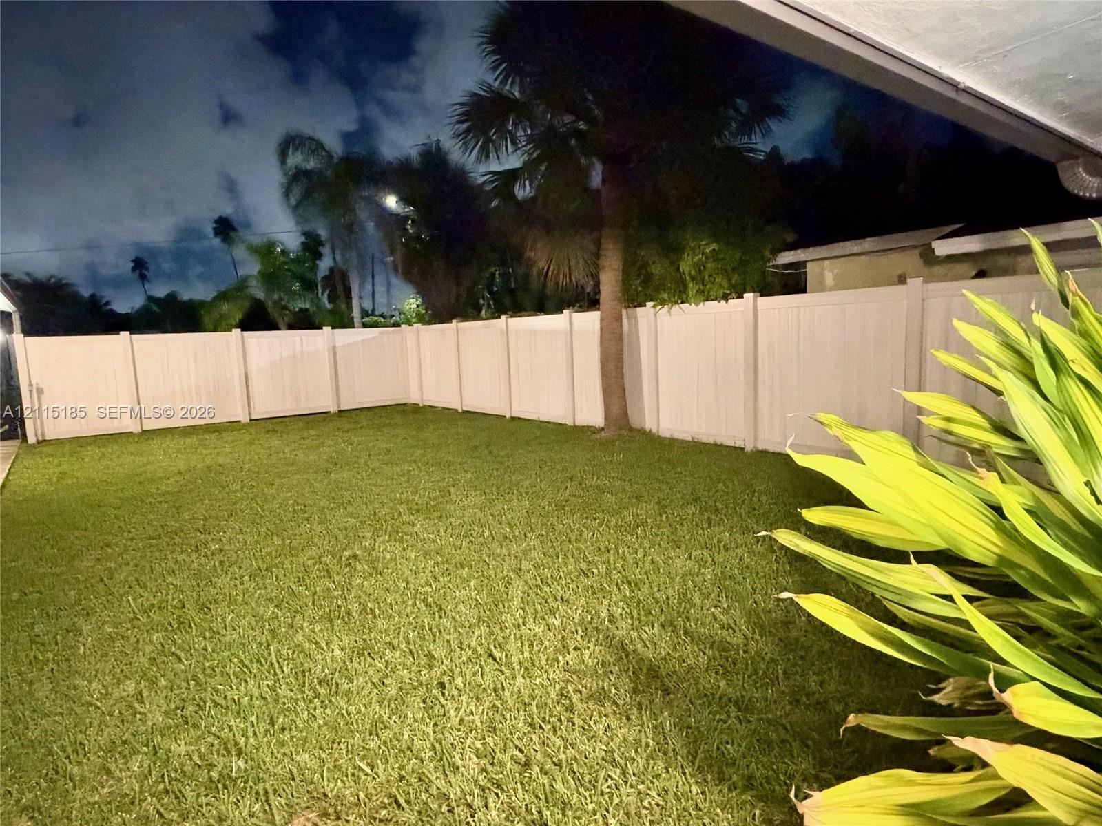Backyard featuring a manicured lawn, full-perimeter white vinyl fencing, and mature palm trees