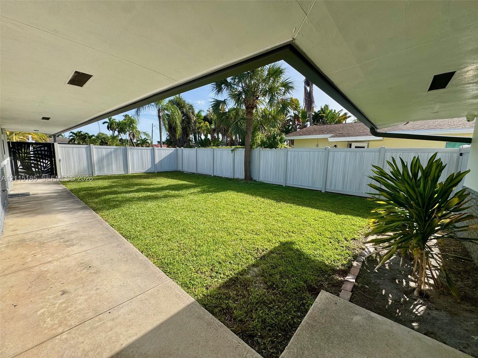 Covered concrete patio, fenced backyard, and mature palm trees