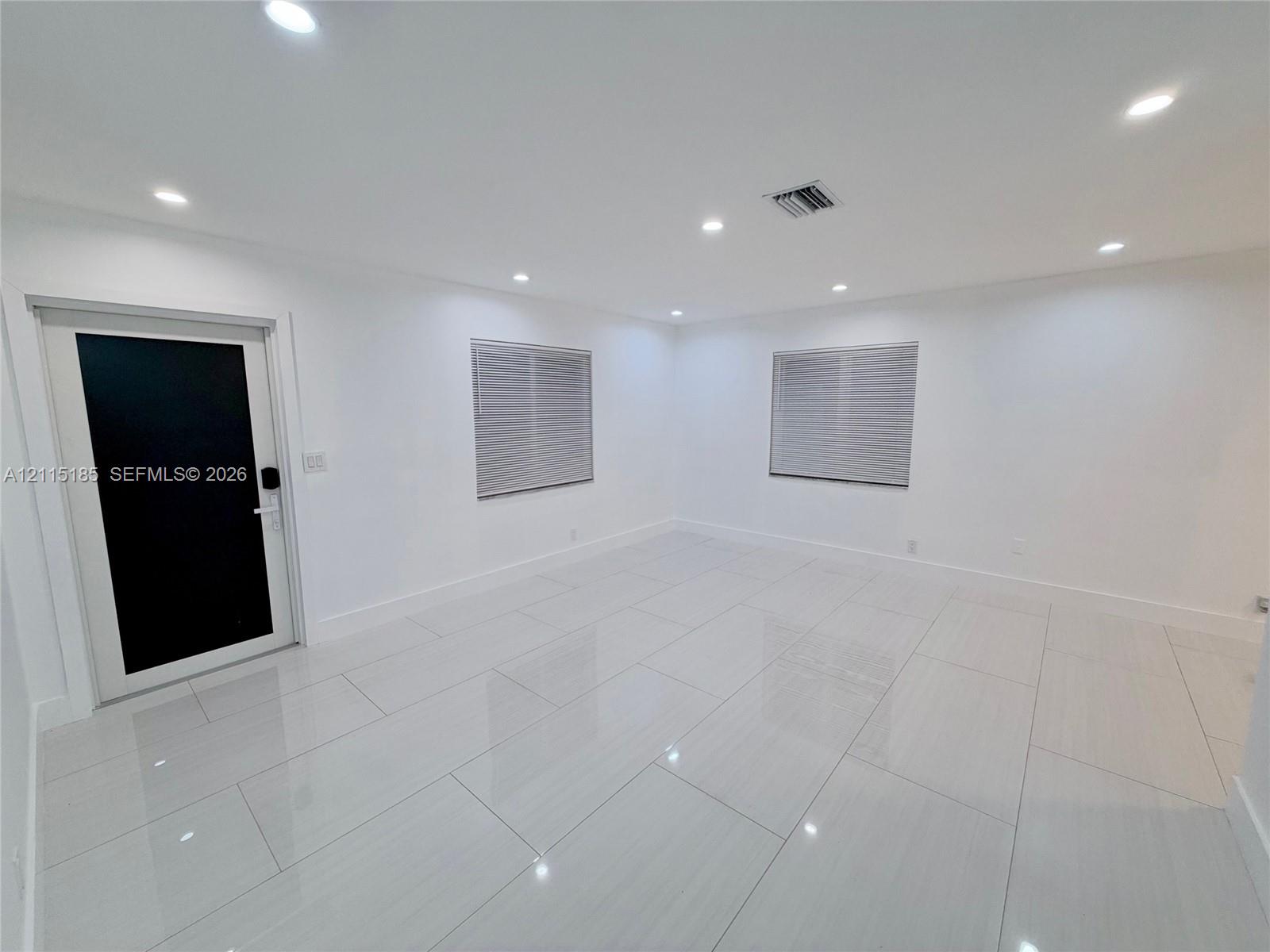 Interior space featuring high-gloss tile flooring, recessed ceiling lighting, and a modern black-paneled entry door with hardware