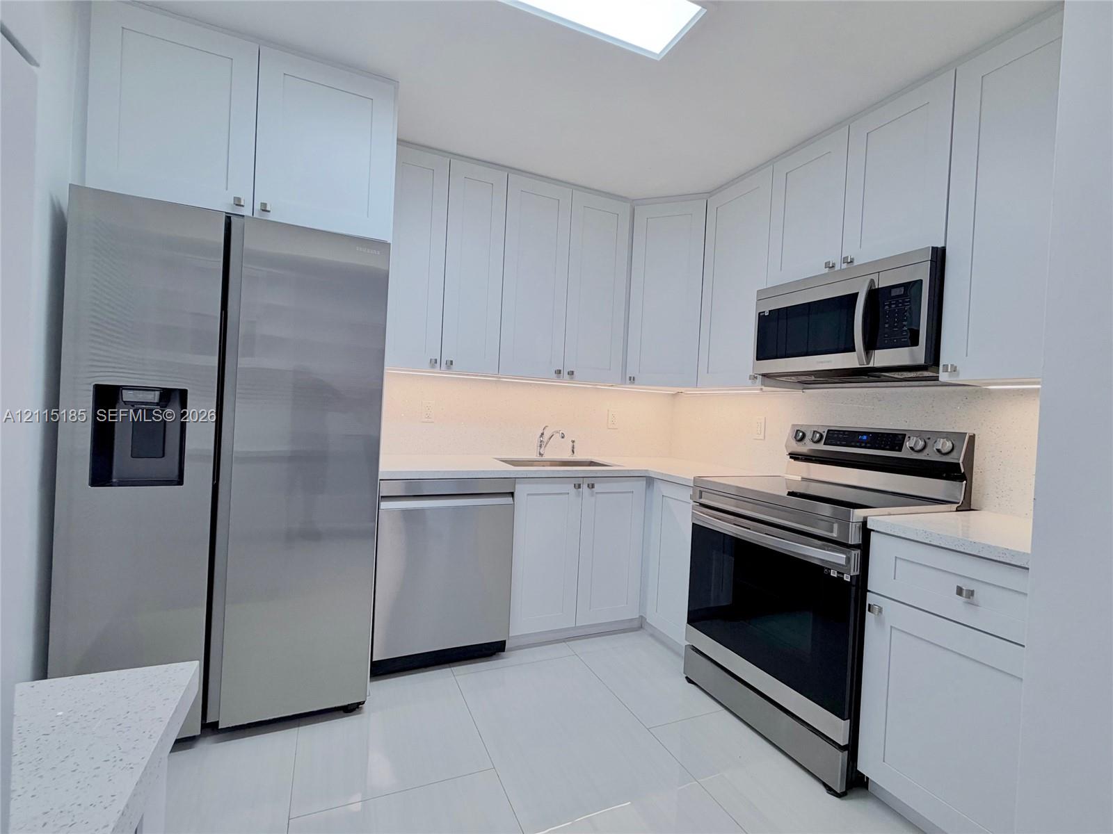 Kitchen featuring white shaker-style cabinetry, quartz countertops, stainless steel appliances, large-format tile flooring, and a recessed skylight