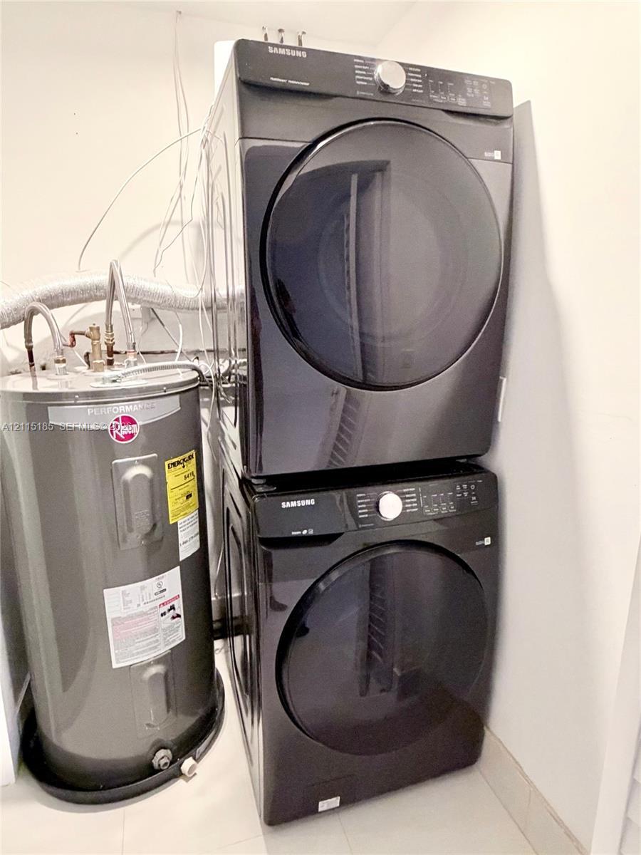 Stacked dark-finish front-load laundry appliances and a cylindrical water heater