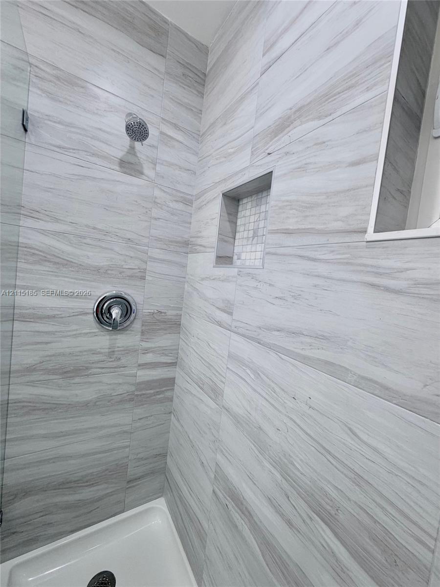 Shower enclosure featuring large-format neutral-toned tile, built-in recessed niche with mosaic accent, glass panel, and polished chrome shower fixtures