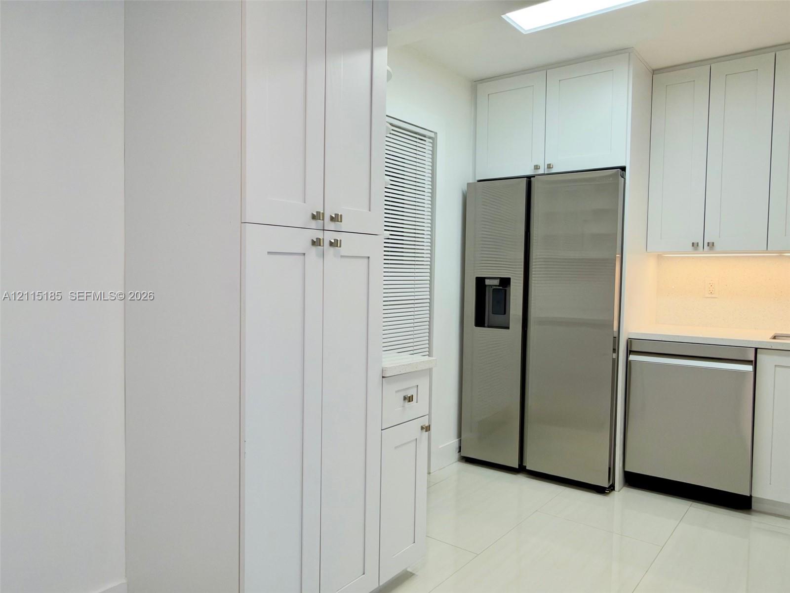 Kitchen featuring white shaker-style cabinetry, stainless steel appliances, polished stone-finish countertops, tile flooring, and a ceiling skylight