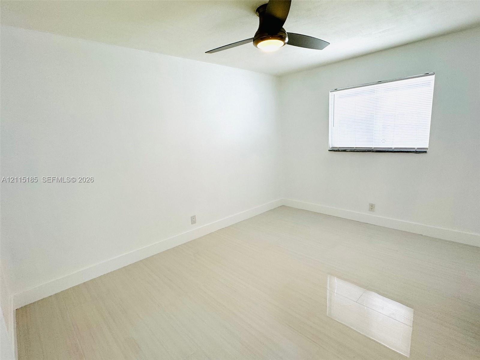 Neutral-toned interior featuring light wood-finish flooring, white walls, and a ceiling fan with integrated lighting