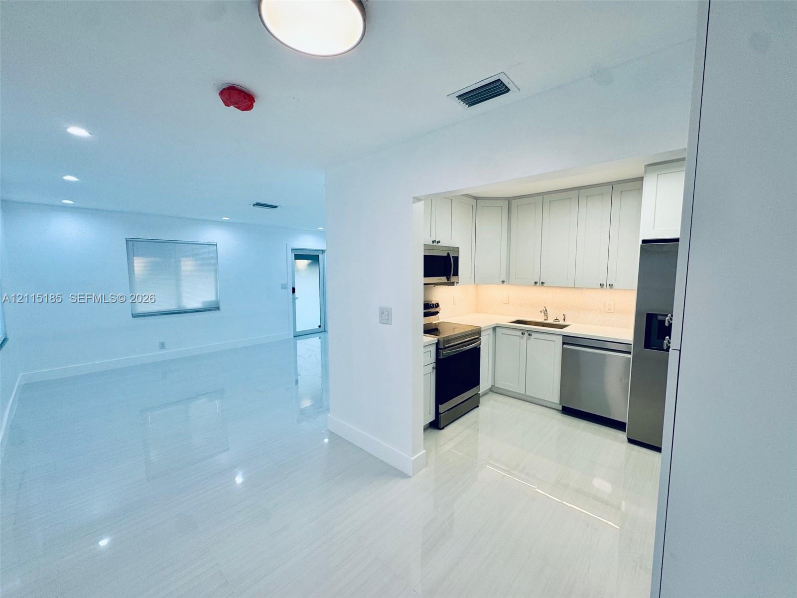 Kitchen featuring white shaker-style cabinetry, solid-surface countertops, stainless steel appliances, and tile flooring throughout
