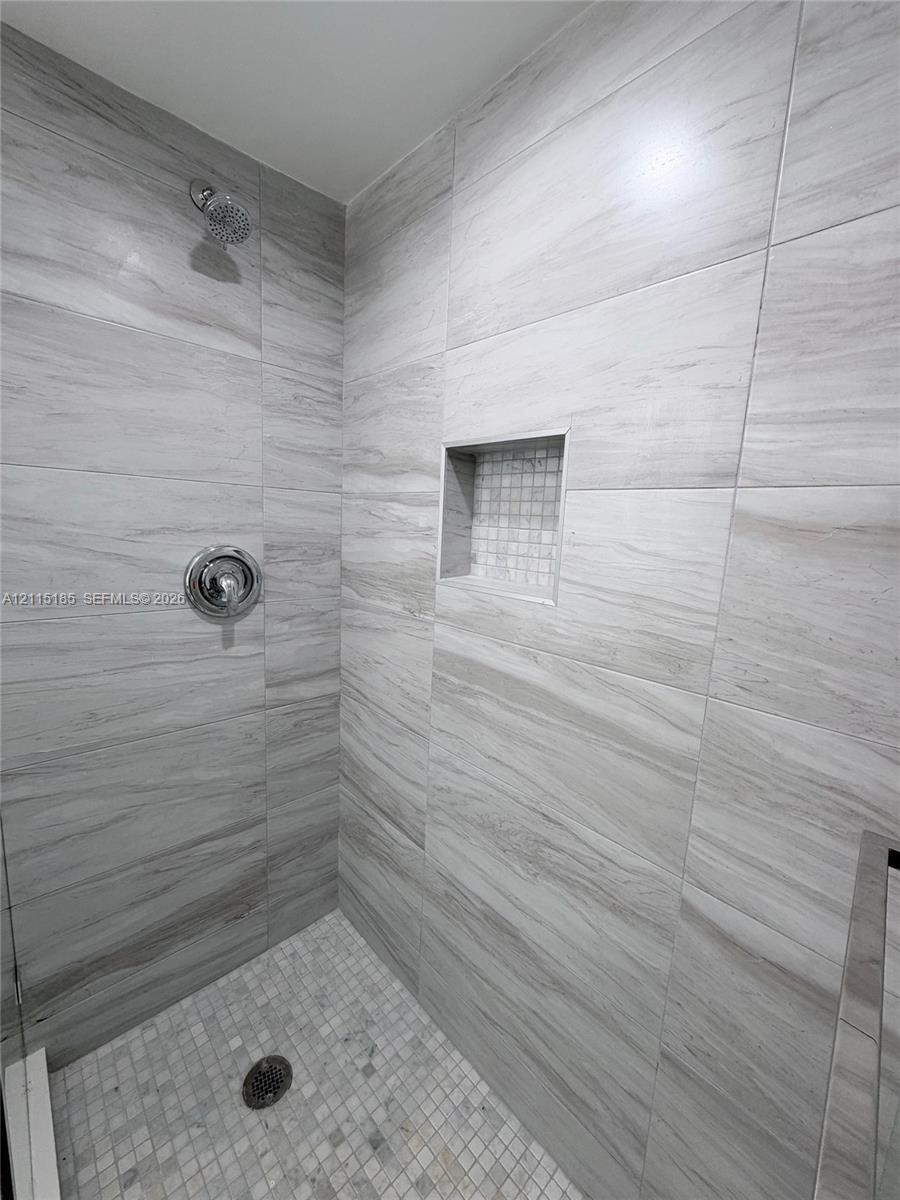 Walk-in shower featuring large-format neutral-toned wall tile, a recessed tiled niche, a mosaic-tiled floor, and a circular shower head with a round control handle