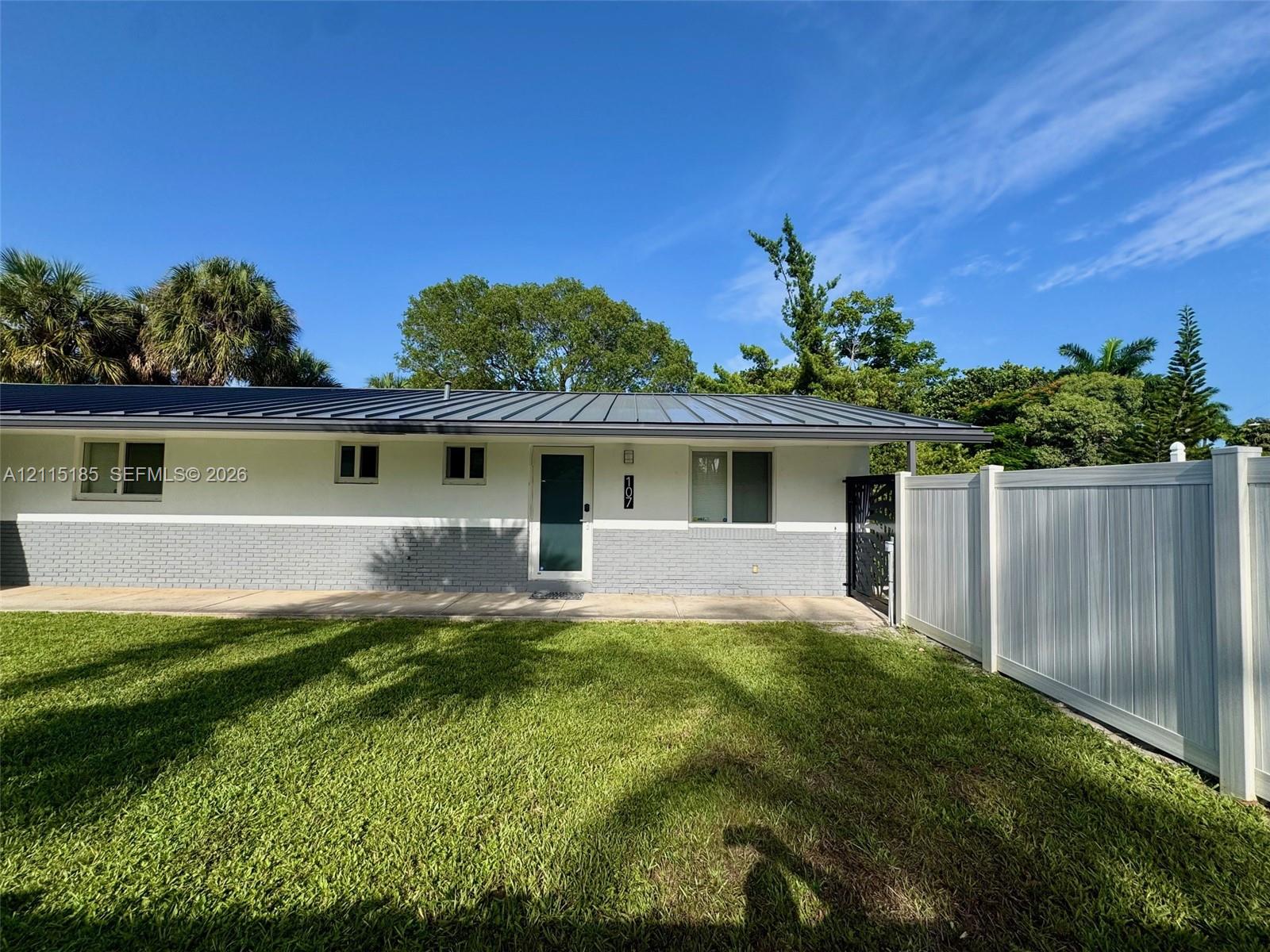 Exterior featuring a metal roof, two-tone masonry and stucco siding, a paved walkway, and a full-height vinyl privacy fence