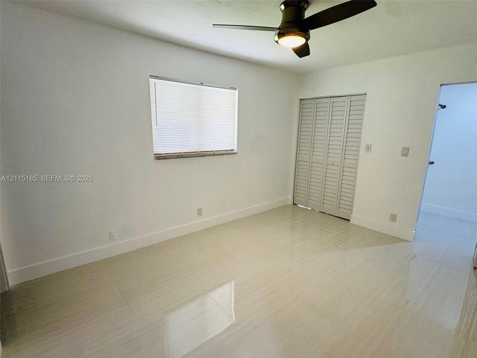 Interior room featuring light-toned tile flooring, louvered bi-fold closet doors, and a ceiling fan with integrated lighting