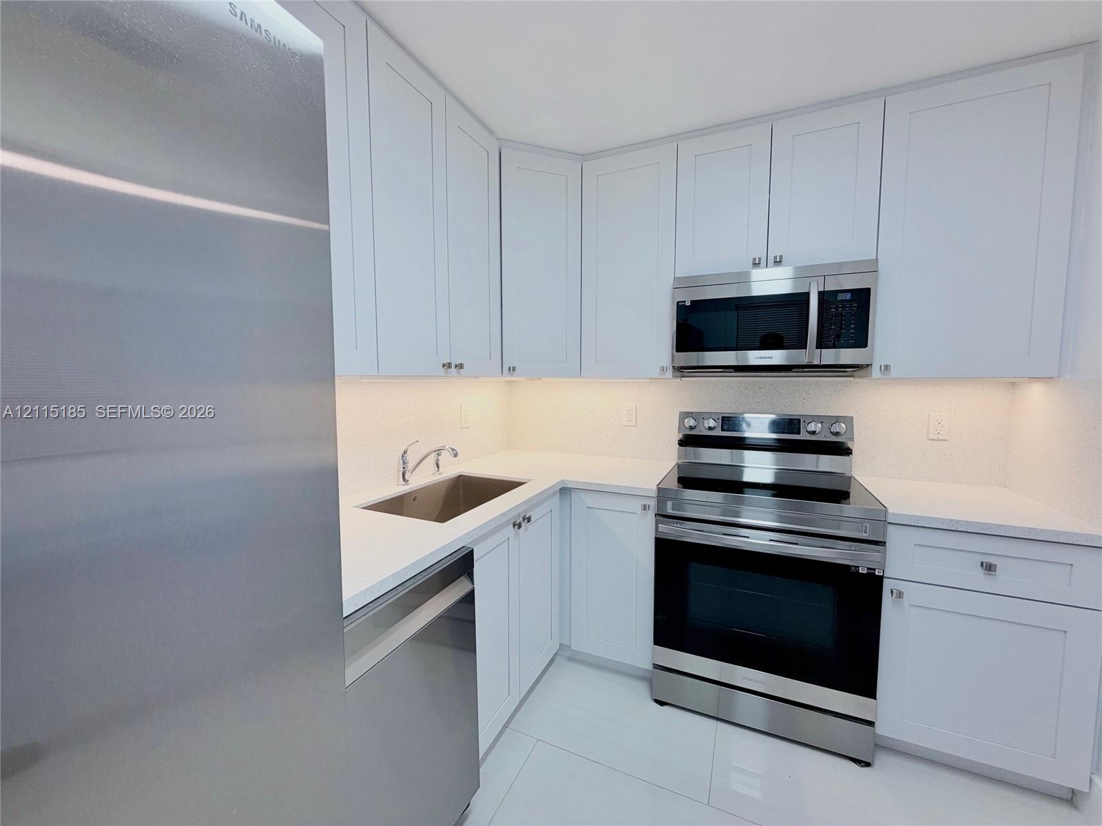 Kitchen featuring white shaker-style cabinetry, stainless steel appliances, white solid-surface countertops, and undermount stainless steel sink